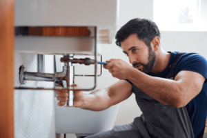 man fixing under sink plumbing to prevent leaks